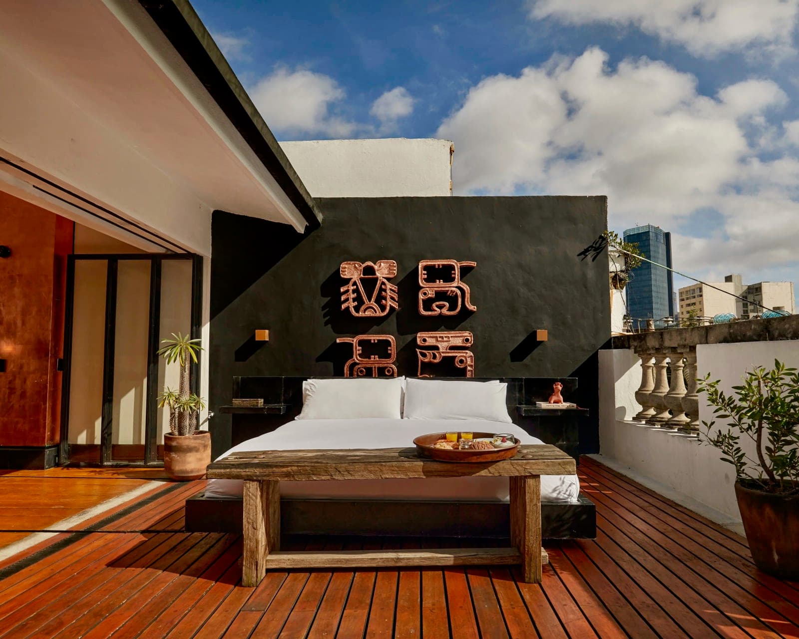 outdoor patio with wood decking, black wall, artwork, and a white linen covered bed outside during day
