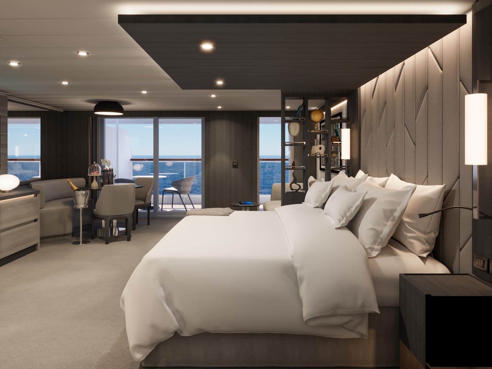 Modern ocean-view cruise ship suite with a king bed dressed in crisp white linens, dark wood and soft grey finishes, built-in shelving, and a seating and dining area leading to a private balcony overlooking the open sea.