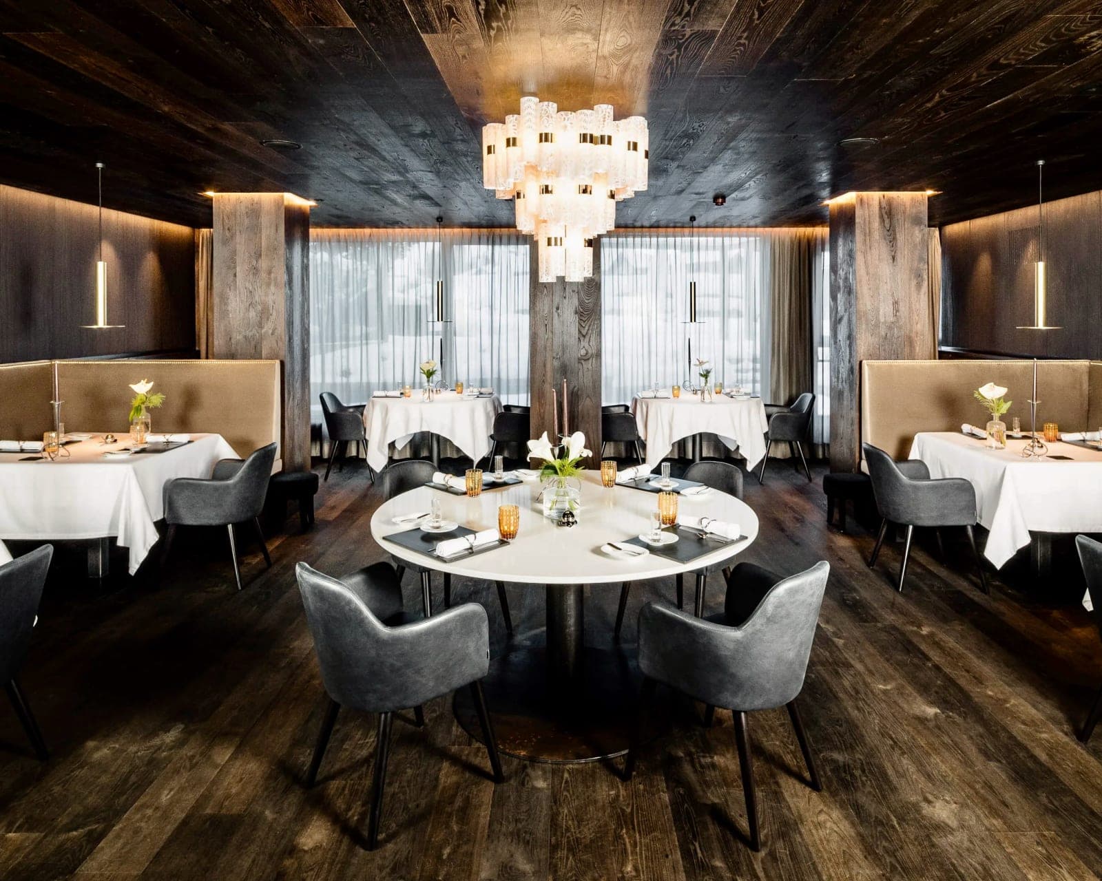 restaurant with white tables, grey chairs, black wood floor and ceiling, and modern chandelier