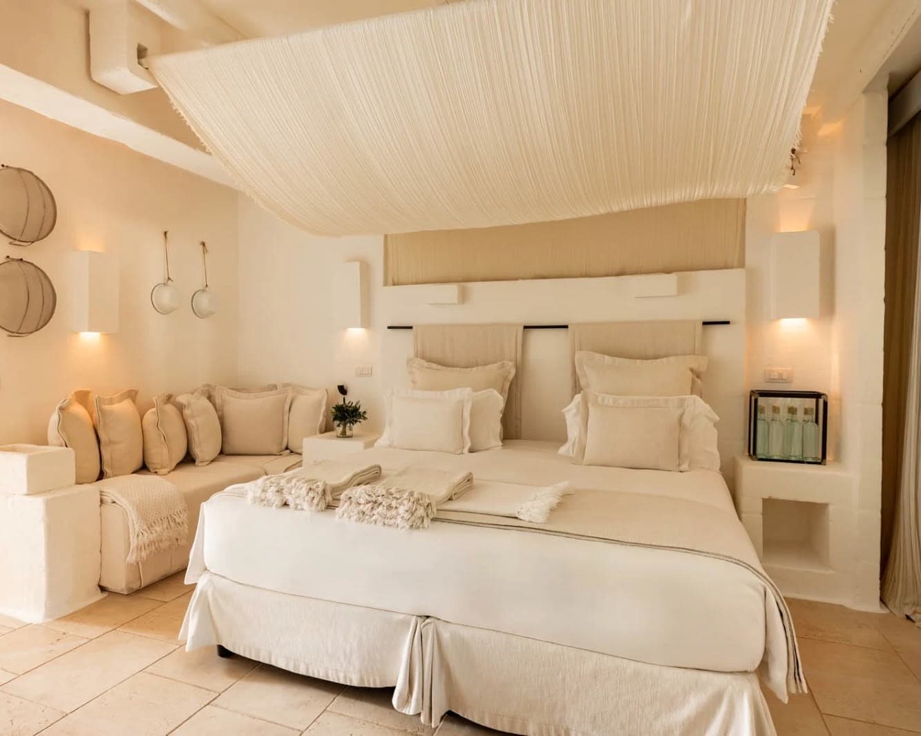 White and beige room with bed, curtain draped above the bed, and sofa off to the side