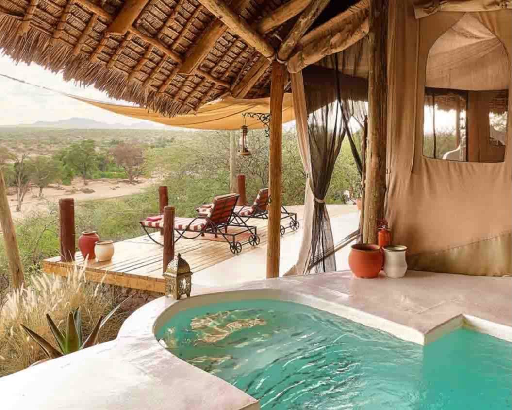 private pool next to tan tent and deck with lounge chairs overlooking green savanna