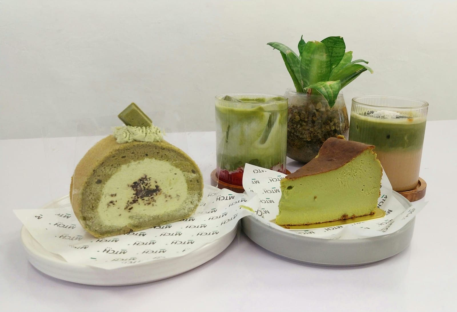 A selection of matcha-flavored desserts on white plates on a white table.