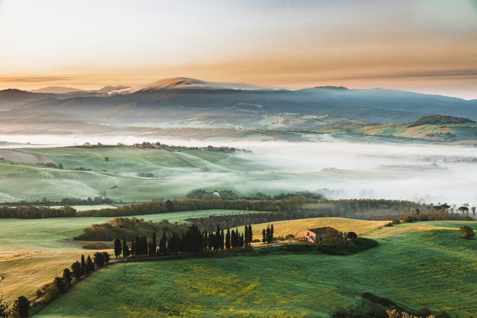 An aerial view of a countryside with rolling green hills, light fog, at dawn or dusk