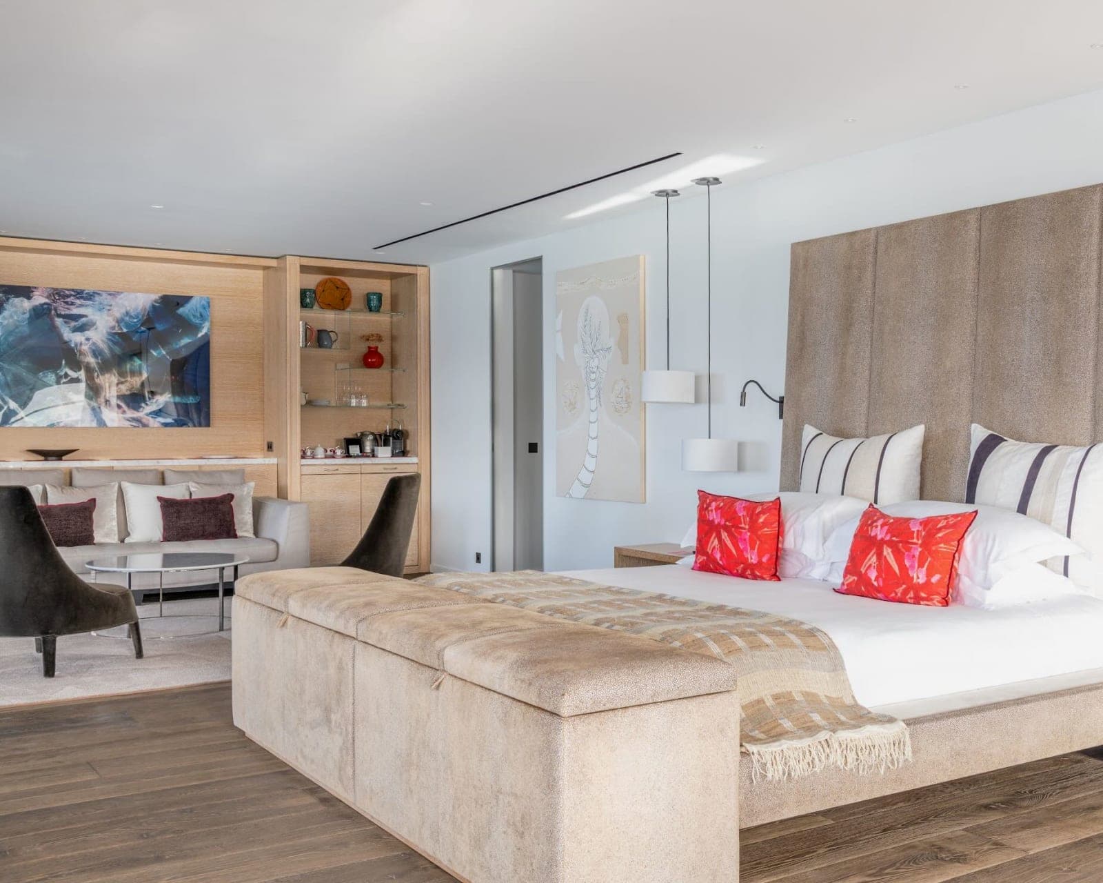 a modern neutral-colored hotel room with bed, wood floor, and seating area beneath artwork