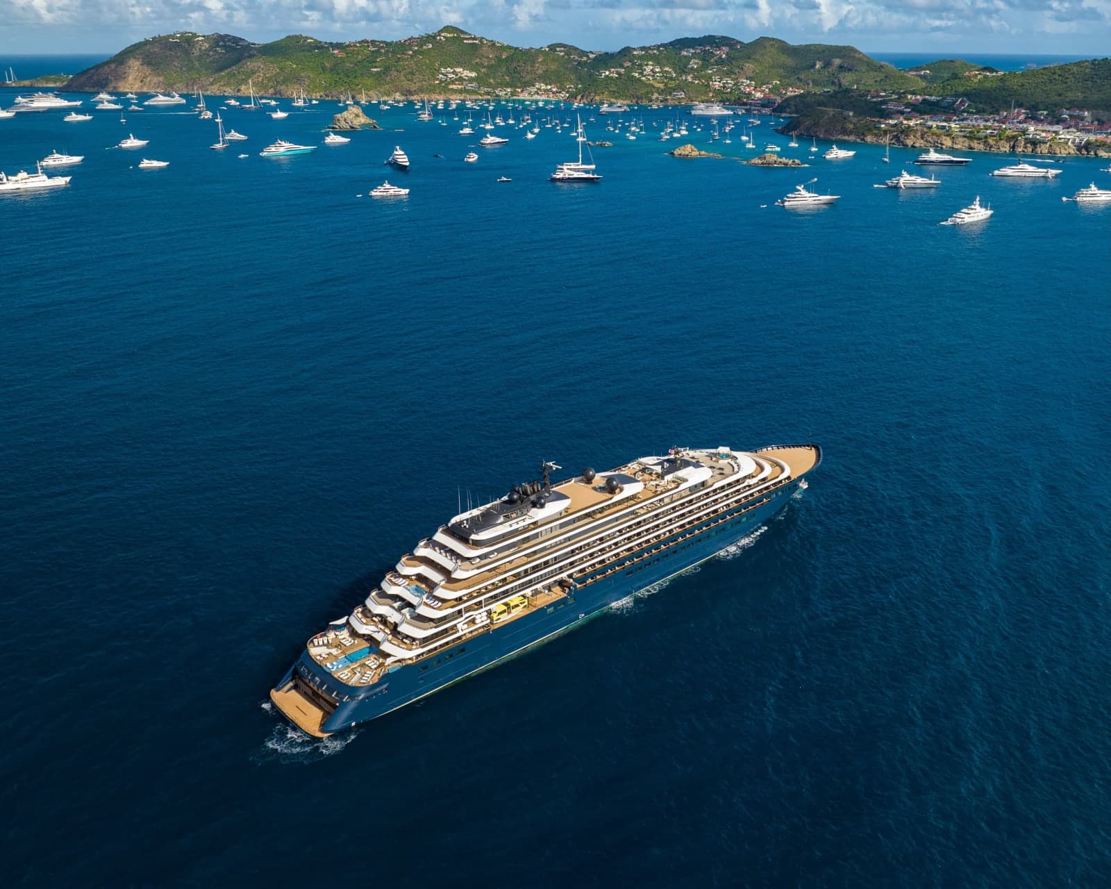 a yacht in turquoise waters off the coast of a tropical island with smaller yachts anchored around it during day